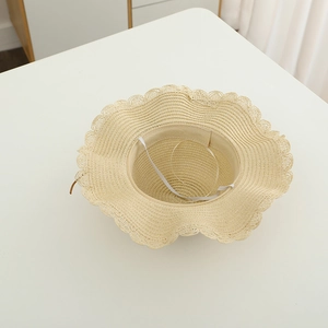 Detailed view of woven straw sun hat with wavy brim and elastic chin strap