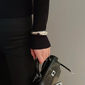 Close-up of a wide polished silver cuff bracelet styled over a black knit sleeve