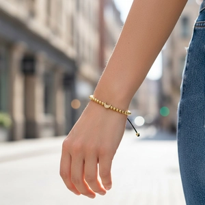 Detail of adjustable gold beaded bracelet featuring a crescent moon charm on a model