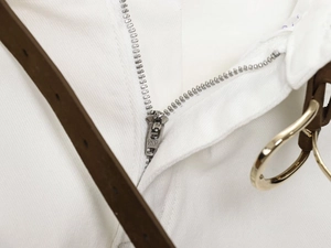 Detail of high-waist white denim pants with metal zipper and slim brown leather belt