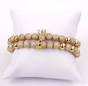 Detailed view of two gold-plated crown bracelets with micro-pave zircons on a white pillow