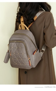Detalle de mochila acolchada topo con remaches llevada por modelo con abrigo marrón