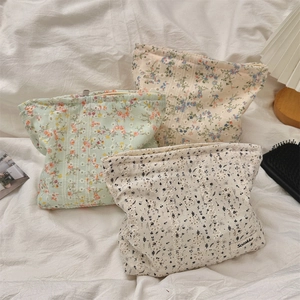 Detail view of floral embroidered canvas makeup bags with zippers on cozy bedding