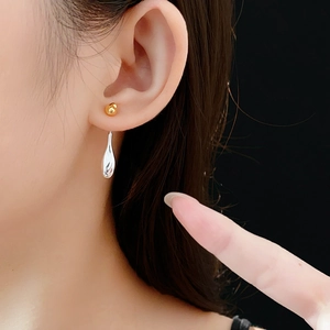 Close-up of minimalist gold ball and silver water drop earrings on model in high detail