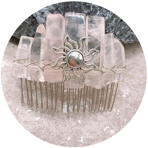 Handmade rose quartz crystal hair comb with silver sun ornament on natural rock background