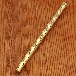 Detail of a golden bamboo-shaped brass pen with Chinese calligraphy on a wooden desk