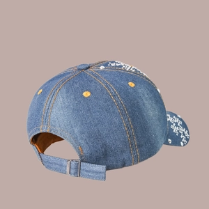 Détail de la casquette en jean bleu avec boucle métallique et broderie de fleurs