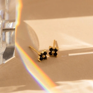 Dettaglio macro di orecchini a quadrifoglio placcati oro con quattro pietre nere a cuore