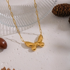 Close-up of 18K gold-plated butterfly pendant with a paperclip chain on a textured surface