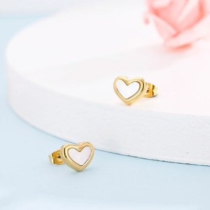 Detail of gold heart earrings with white shell inlay on a minimalist white platform