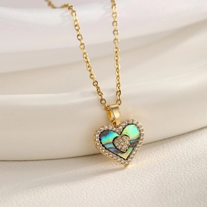 Macro detail of gold necklace featuring double-layered heart pendant with shell and zircon