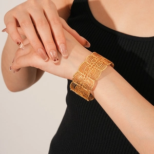 Nahaufnahme eines breiten goldenen Armreifs mit geometrischem Hohlmuster am Handgelenk