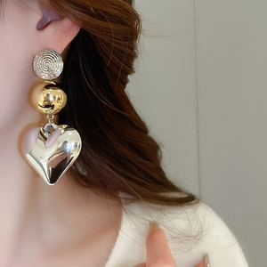 Detailed view of layered silver heart earrings with gold beads on model's side profile