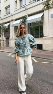 Street style shot of green plaid ruffle sleeve blouse paired with white wide-leg trousers
