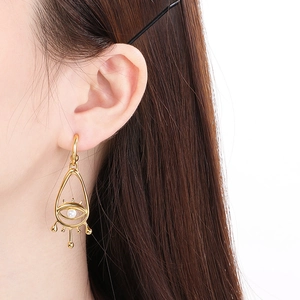 Gros plan de boucles d'oreilles œil maléfique dorées avec perle sur un mannequin