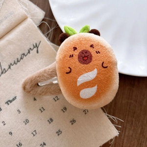 Close-up of a plush orange squirrel hair clip with green leaf detail on a wooden surface