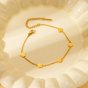 Detail of gold flower charm bracelet with lobster clasp on white ceramic plate