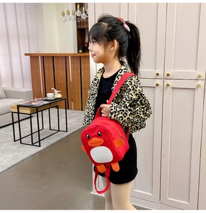 Young girl wearing a cute red cartoon penguin backpack in a bright home interior
