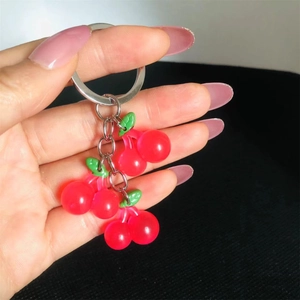 Close-up of translucent red resin cherry keychain with green leaves held by a hand
