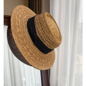 Flat top straw boater hat with black ribbon trim hanging on a wooden stand