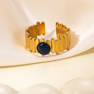 Macro shot of gold textured ring with round blue gemstone on beige silk fabric