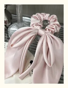 Close-up of a pink satin bow hair tie with smooth silky texture and glossy finish