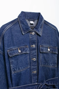 Detail of blue denim jacket showing lapel collar, buttons, and waist belt design