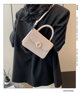 Fashionable beige crossbody bag with gold round clasp worn by model in black suit