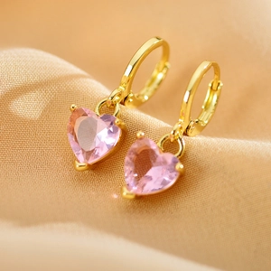 Close-up of gold heart earrings with pink zircon stones on soft beige fabric background