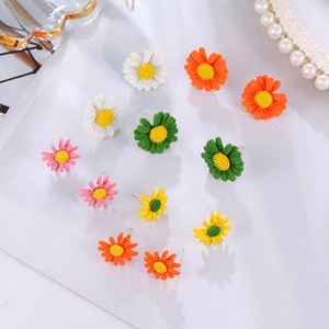 Macro detail of colorful daisy stud earring set in white, pink, and green finishes