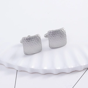 Macro detail of silver square cufflinks with hammered texture on a white shell tray