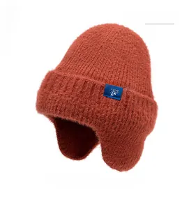 Détail du bonnet en tricot rouge brique avec protège-oreilles et écusson flocon bleu