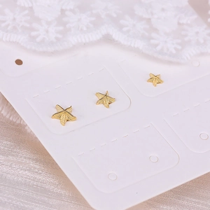 Macro shot of three golden starfish stud earrings on display card with white lace background