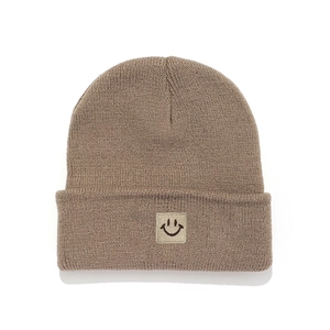 Detail of a brown knitted beanie with a square smiley face patch on the folded brim