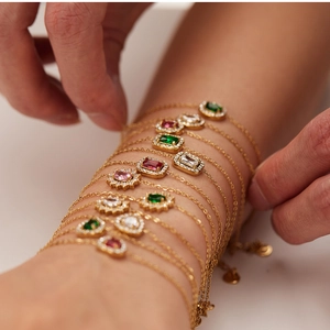 Close-up of stacked gold chain bracelets with colorful heart and square zircon stones