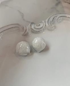 Détail de boucles d'oreilles boules blanches à texture spirale sur un plateau vintage chic
