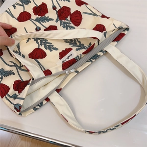 Detail view of cotton tote bag with red floral print, metal zipper, and brand label