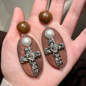 Détail macro de boucles d'oreilles en bois avec croix en métal argenté et strass cœur