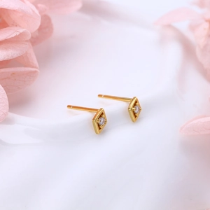 Close-up of gold geometric rhombus stud earrings with single zircon on floral background