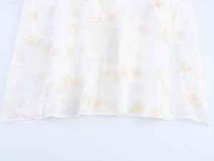 Dettaglio del ricamo dorato con fiori e uccelli su tessuto in chiffon bianco dell'abito