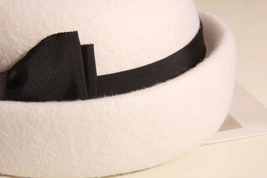 Dettaglio macro di un cappello in feltro di lana bianco sporco con fiocco in nastro nero
