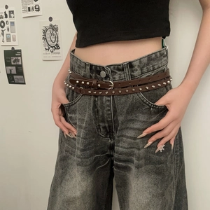 Ceinture punk marron foncé en cuir avec rivets argentés sur un jean large gris délavé