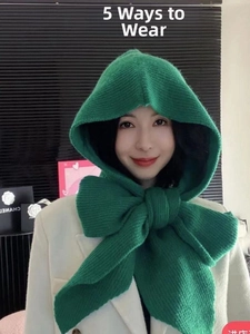 Detail of dark green knit balaclava scarf with a large decorative bow tied at the neck