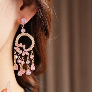 Detail of gold tassel earrings featuring pink teardrop gems on a female model