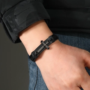 Close-up of woven leather bracelet with metal cross pendant featuring religious text