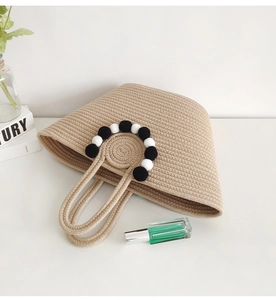 Detail of handmade straw tote bag with black and white pom-poms on circular handle