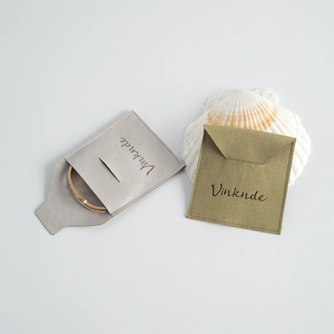 Bolsa de microfibra para joyas en gris y verde con pulsera dorada y una concha