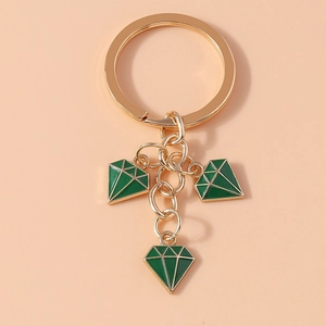 Close-up of golden keychain with three green enamel diamond-shaped pendants on warm background
