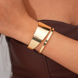 Close-up of a wide polished gold metal cuff bracelet with asymmetrical wrap design
