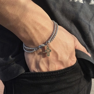 Close-up of double-layer stainless steel cross bracelet on a male wrist with black jeans